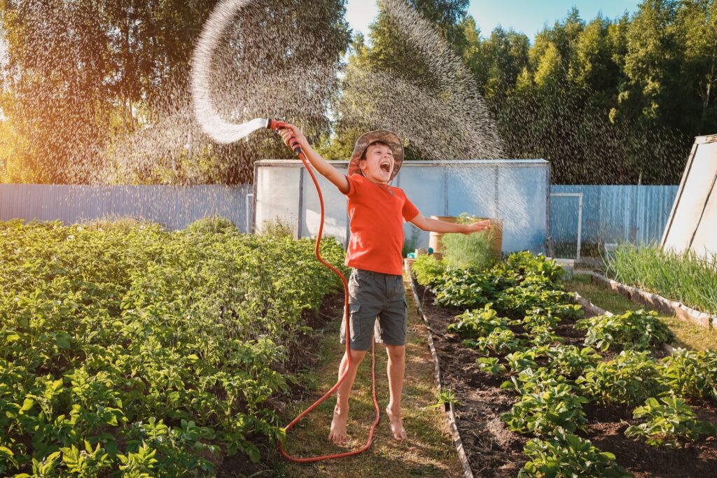 Boy,Child,Jumping,Splashing,Hose,Water,In,The,Backyard,In