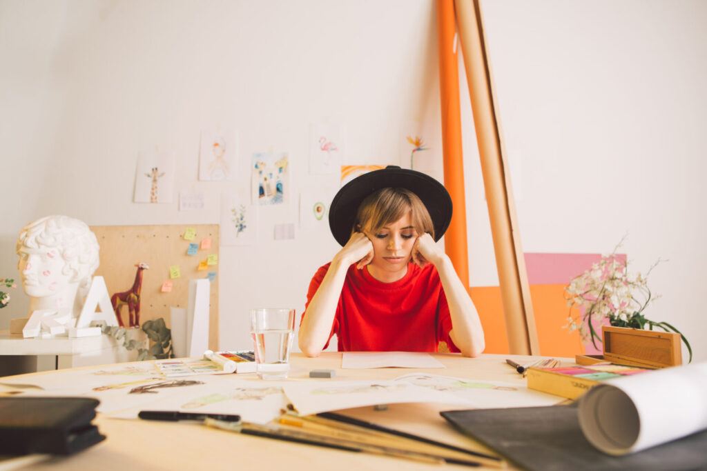 Sad,Girl,Illustrator,Artist,Clutched,Head,Sitting,At,Table,In