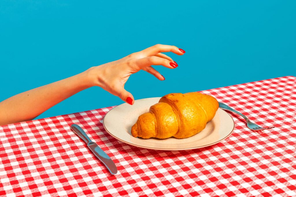 French,Breakfast.,Female,Hand,Tasting,Crispy,Croissant,On,Plaid,Tablecloth