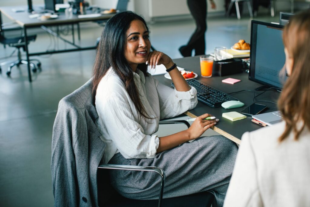 Side,View,Of,Smiling,Businesswoman,Talking,To,Colleague,While,Sitting