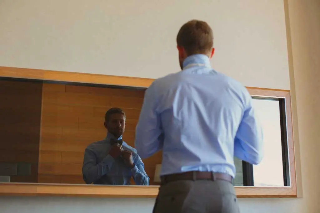 man ties bowtie in mirror 2166075111