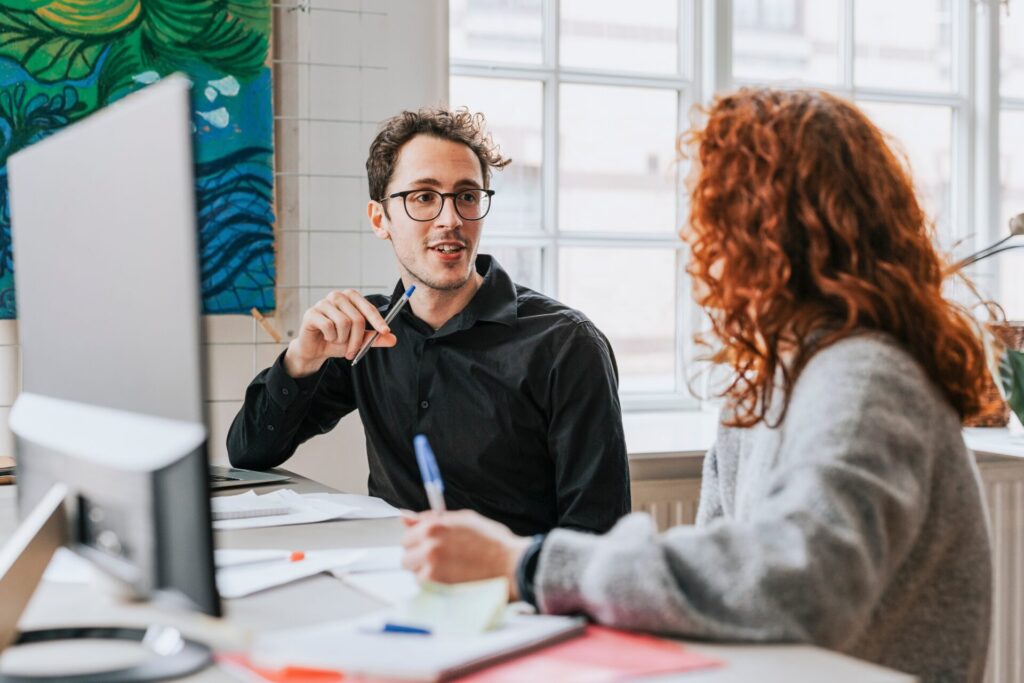 Businessman,Discussing,With,Female,Redhead,Colleague,At,Desk,In,Office