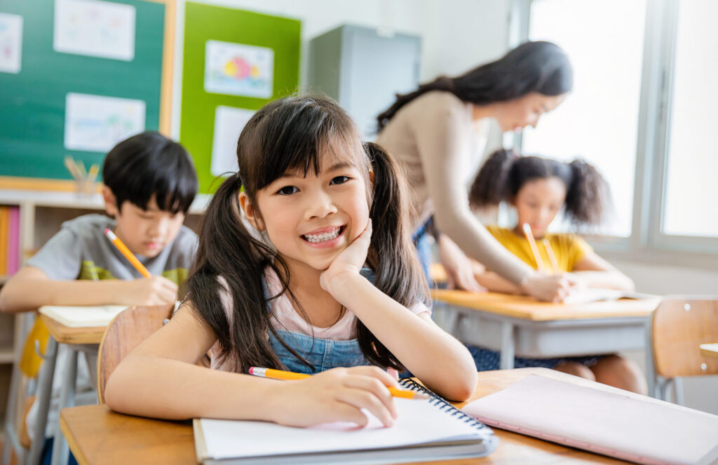 Portrait,Of,Smile,Little,Pupil,Writing,At,Desk,In,Classroom